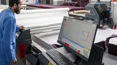 Male operator in a blue coat actively monitoring the digital control console of a large automated cutter.