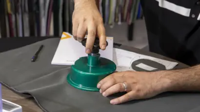 Close-up of a quality control technician using a circular fabric cutter to test the GSM (grams per square meter) of grey textile.