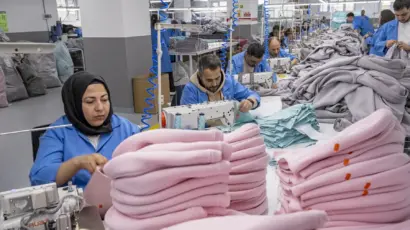 Female worker neatly stacking and organizing finished garments at the end of the production line.