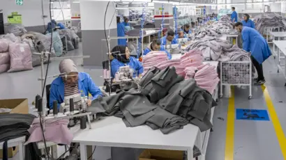Workers in blue uniforms diligently sewing fabrics at their respective stations.