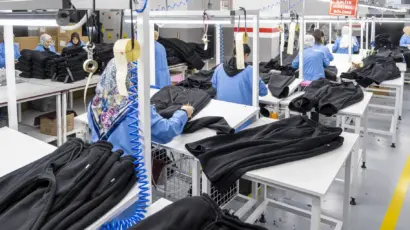 A line of quality control specialists efficiently processing and inspecting bulk black apparel in a bright factory setting.