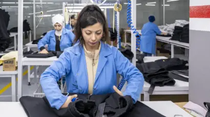Quality control worker closely inspecting the interior seams and finish of a black garment on the production floor.