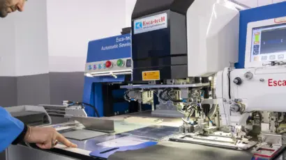 Operator adjusting a computerized pattern sewing Esca-tech machine used for detailed garment construction.