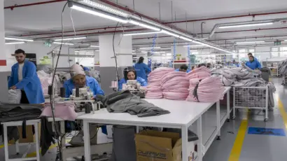 Wide shot of the sewing floor at Istanbul Factory showing multiple workers in blue coats assembling garments.